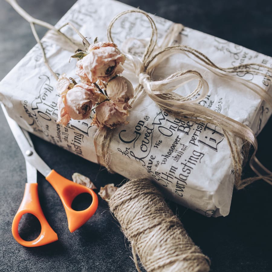 Christian wrapping paper on wrapped present with dried flowers next to scissors and twine