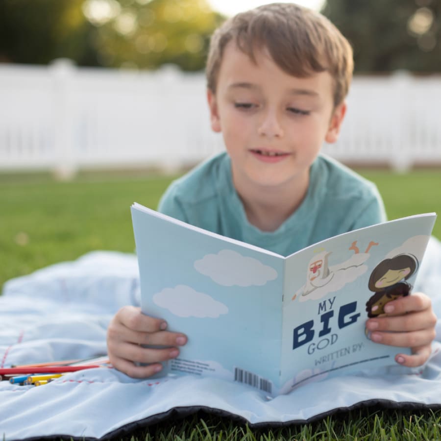 boy reading his bible journal for kids outside on a blanket on grass
